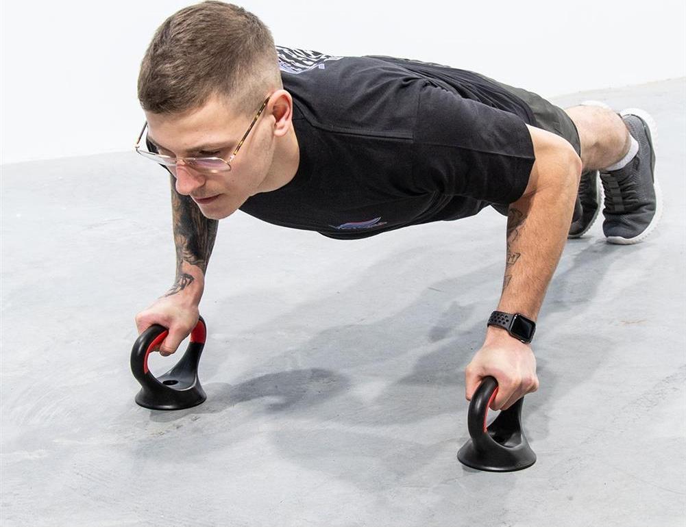 Hantler i svart og rødt plast brukes til push-ups, sett fra siden med fokus på grep og stabilitet på gulvet.