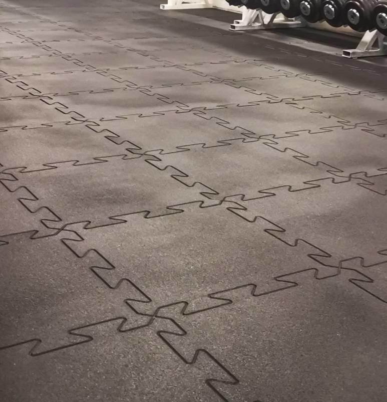 Gummigulv med sammenkoblede, mørkegrå puslespillfliser og kanter, sett skrått ovenfra, for hjemmegym.