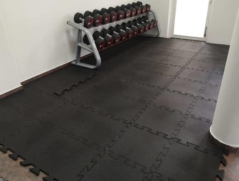 Treningsgulv i svarte, sammenleggbare puslespillmatter lagt ut i hjemmegym med manualstativ i bakgrunnen.