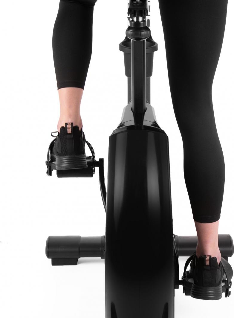 Trimsykkel sett bakfra med person iført svarte sko og tights, føttene festet i pedalene på sykkelen.