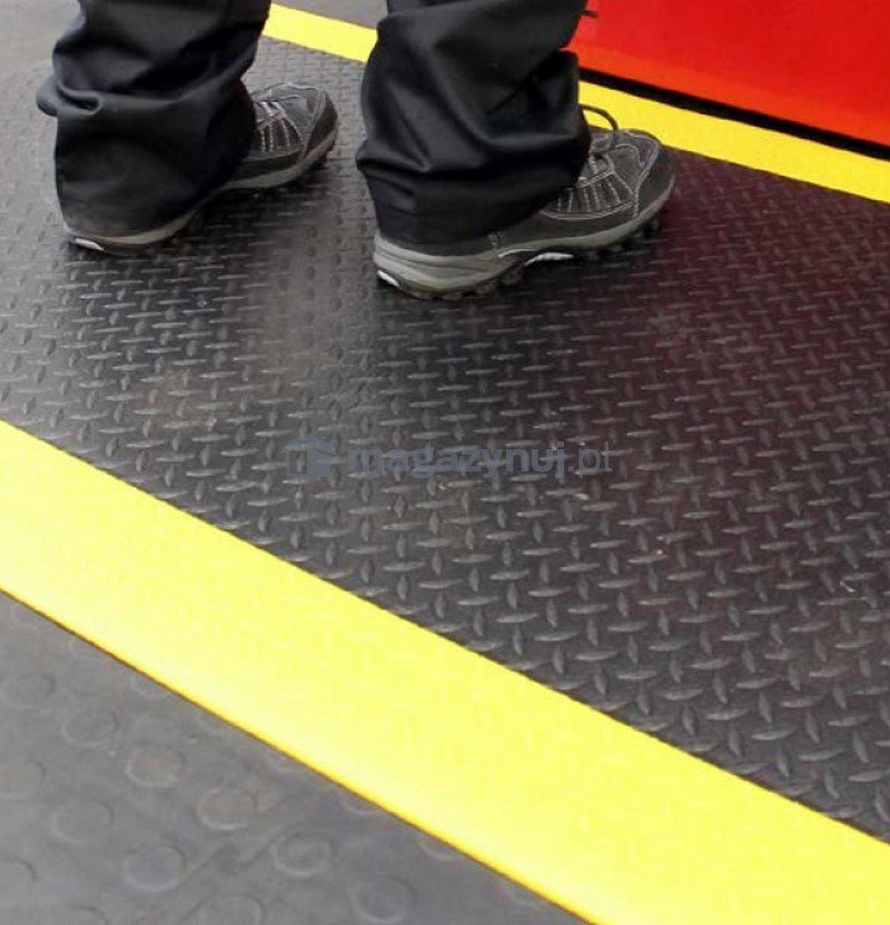 Verksted Matte med sklisikkert mønster og gule kanter, sett ovenfra med sorte sko plassert på matten.