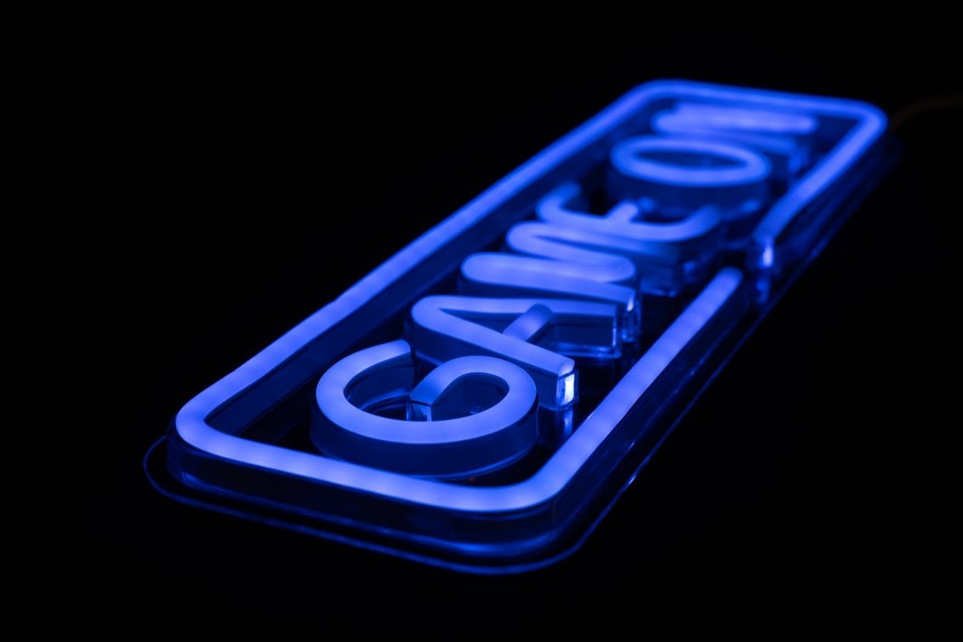 Tredemølle Neonskilt Game On blå LED-lys, sett fra siden mot mørk bakgrunn.