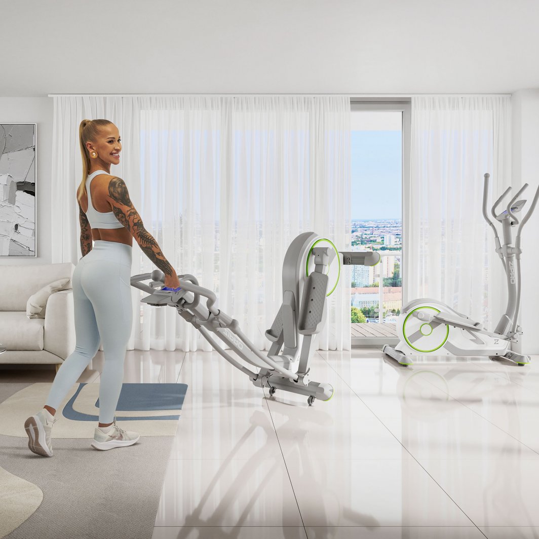 Ellipsemaskin Trening kvinne i lyst treningstøy triller grå ellipsemaskin med grønne detaljer i lys stue.