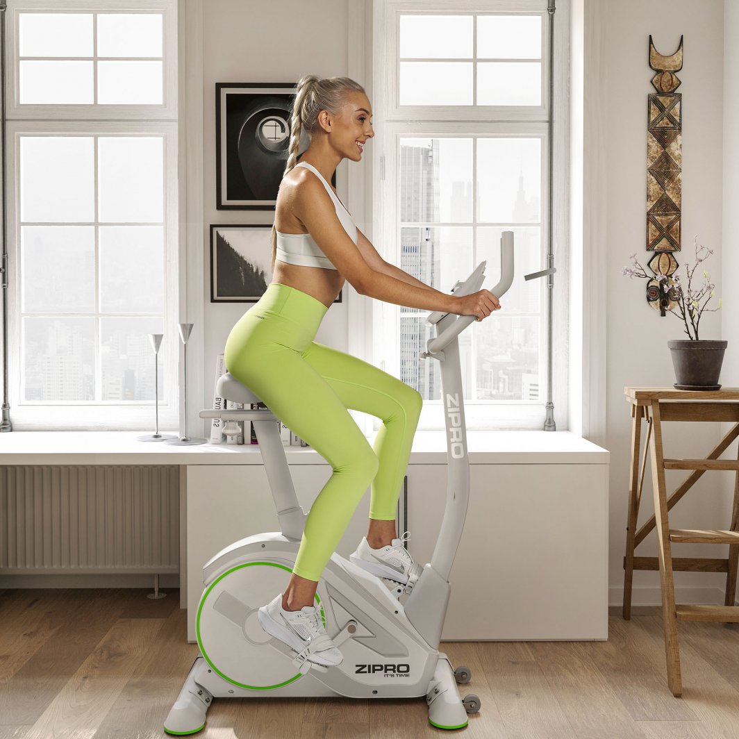 Ergometersykkel i lysegrått med grønne detaljer, dame trener på sykkelen i lys, moderne stue.