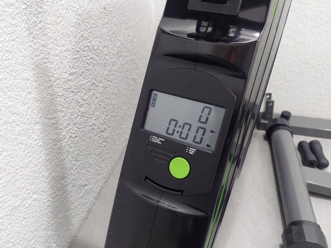 Romaskin Trening med digitalt LCD-display, knapp og funksjoner, sort plast og grønne detaljer, sett fra siden.