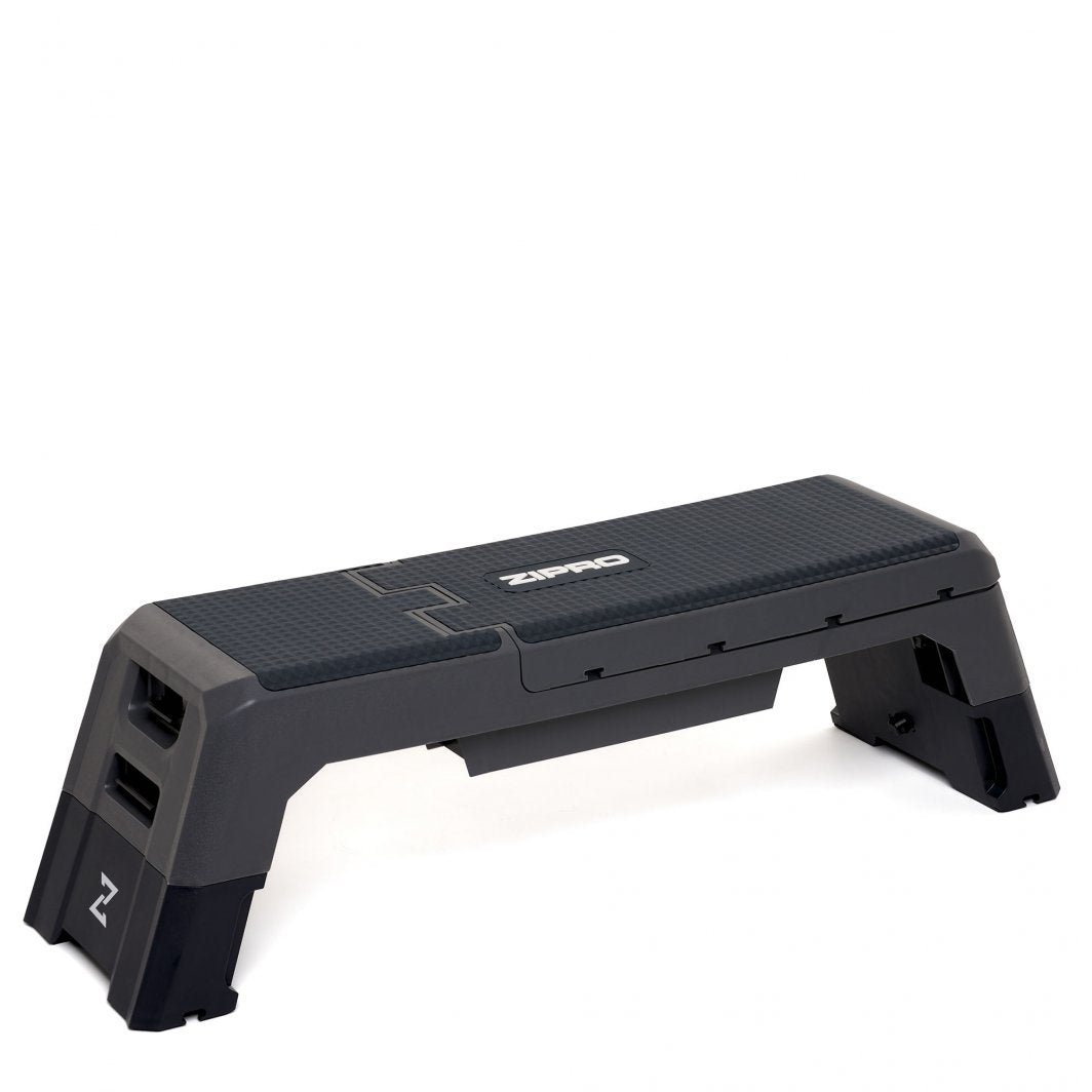 Multifunksjonell Treningsbenk i sort plast med grå detaljer, strukturert overflate og justerbare bein, sett skrått.