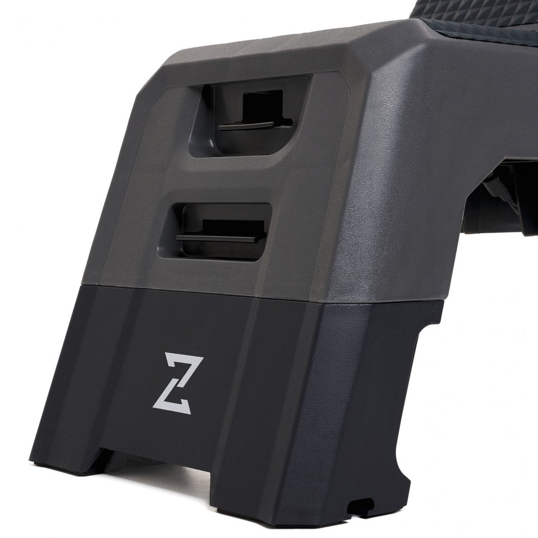 Multifunksjonell Treningsbenk i sort og grå plast med Z-logo, sett fra siden, viser håndtak og låsemekanismer.