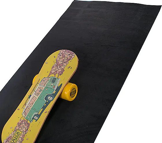 Treningsmatte med stort, sort underlag og skateboard med gul underside og grønn bil-illustrasjon, sett skrått ovenfra.