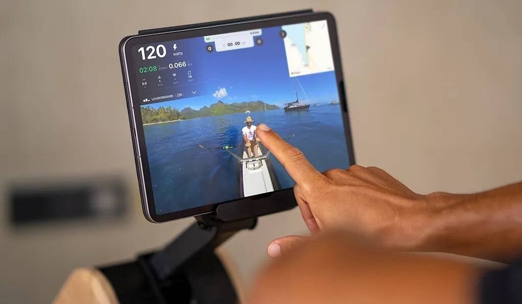 Romaskin Trening med stor skjerm som viser naturvideo, statistikk og kart mens en hånd trykker på skjermen.