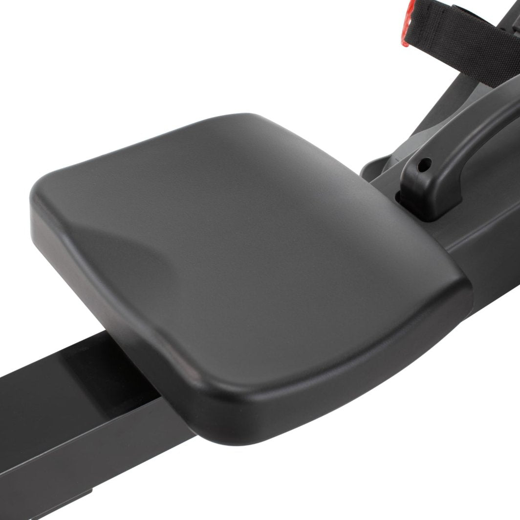 Romaskin Sammenleggbar sete i sort plast med avrundede kanter, montert på skinne med feste og stropp synlig.