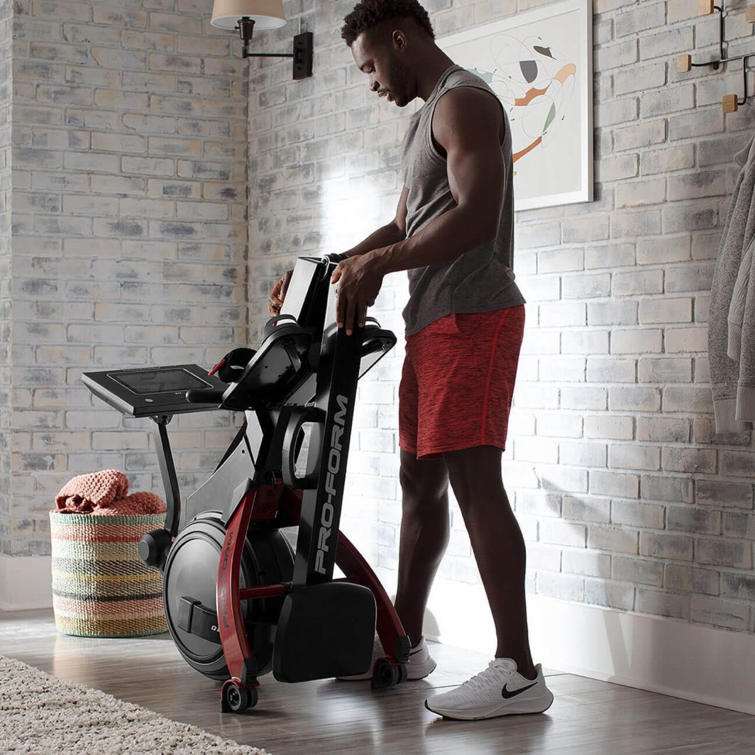 Romaskin Trening sammenleggbar modell i sort og rødt, vises fra siden mens en person folder den sammen.