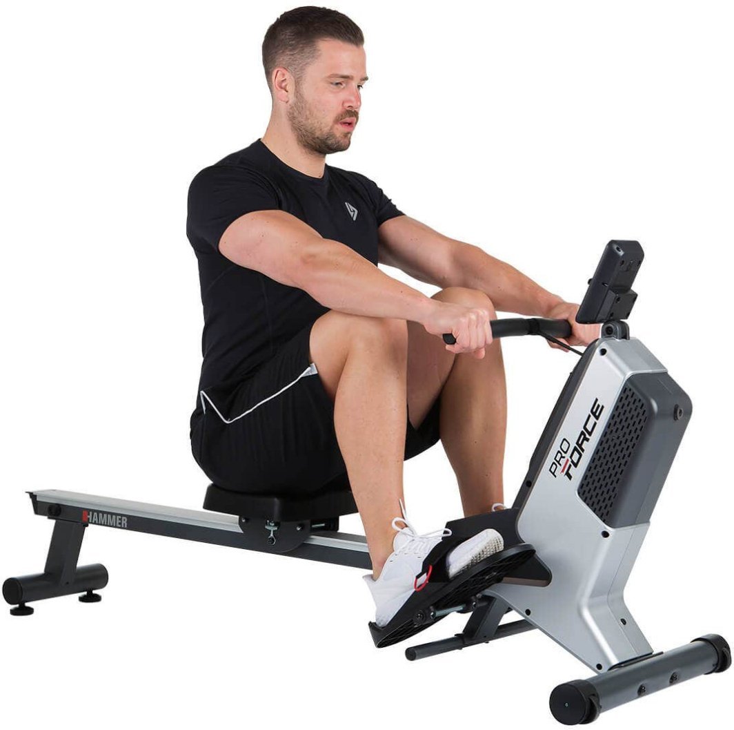 Treningsmaskin i sølv og sort, en mann i treningsklær ror, med synlige pedaler og elektronisk display.