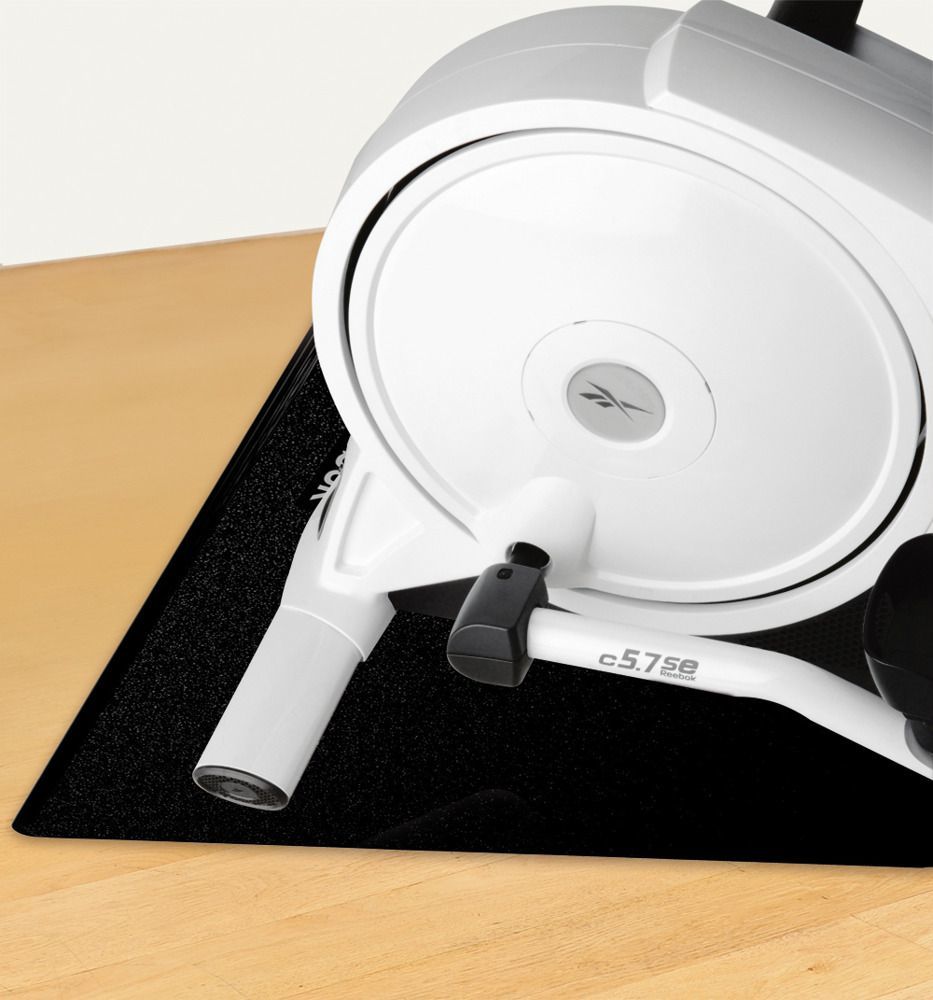 Beskyttelsesmatte under hvit treningsmaskin med sirkulær konstruksjon, plassert på lyst tregulv.