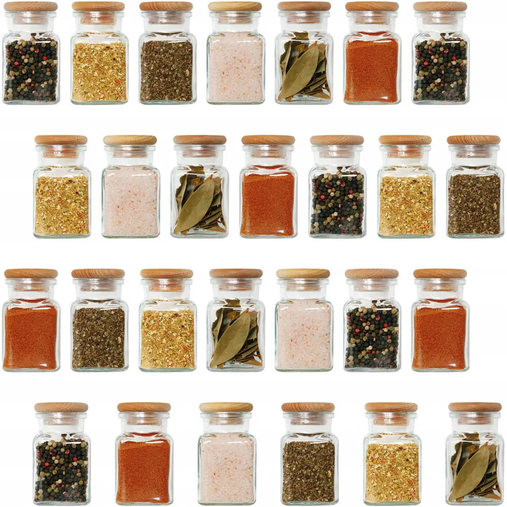 Krydderglass med lyse trekorker, fylt med ulike krydder, stilt opp i rekker mot hvit bakgrunn.