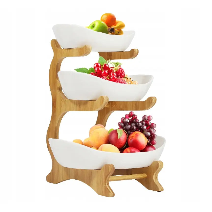 3-etasje fruktkurv og grønnsaksstativ med tre hvite skåler fylt med frukt i lyst trestativ, skrå vinkel.