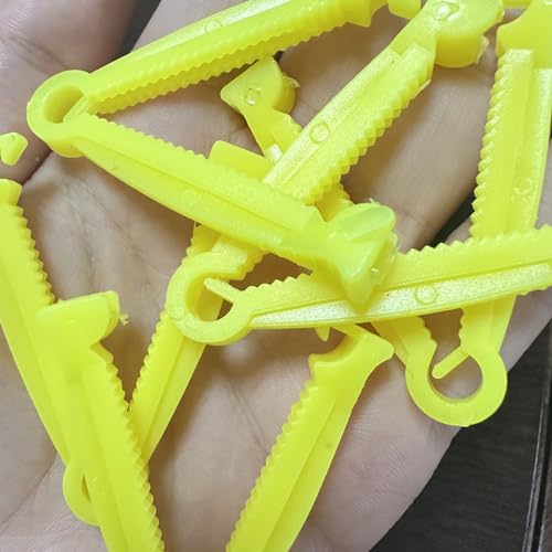 Valpesett med flere gule navleklemmer i plast, taggete kanter og små åpninger, holdt i en hånd.