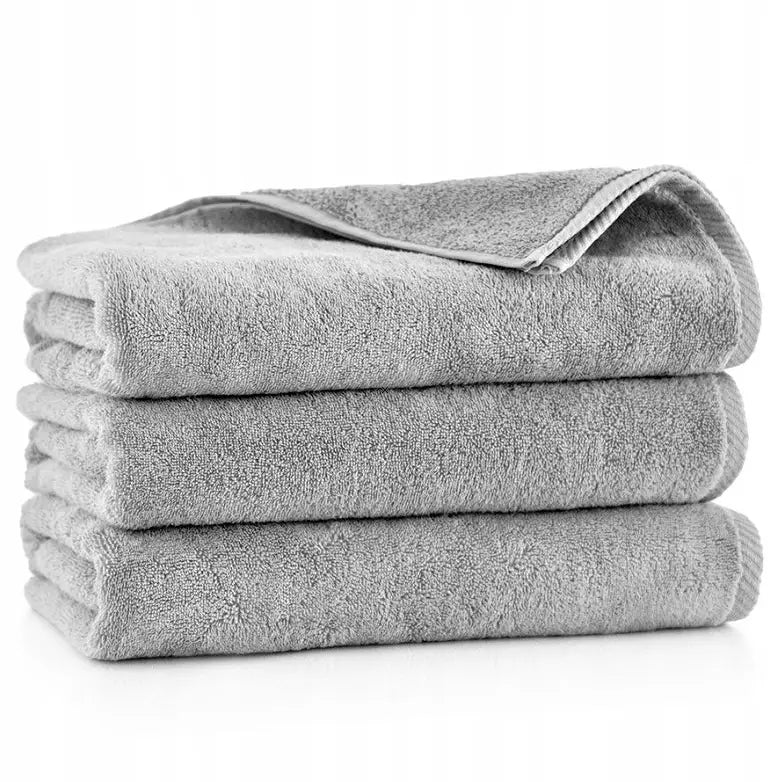 Grå frottéhåndklær, sett fra siden, øverste håndkle med brettet hjørne mot hvit bakgrunn.