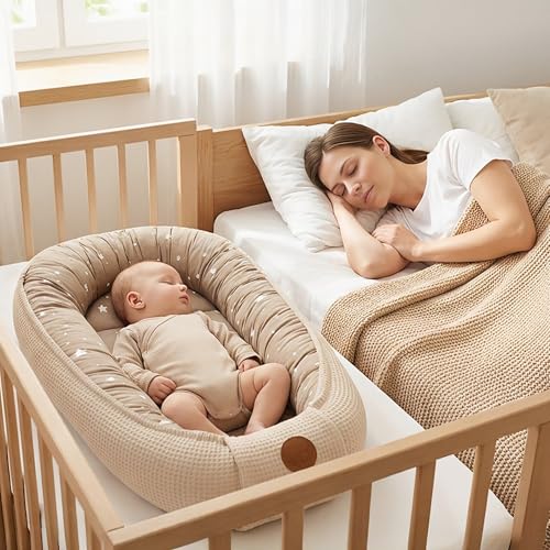 Babynest 50x90cm i beige med stjernemønster, spedbarn ligger i nestet i sprinkelseng ved siden av sovende voksen.
