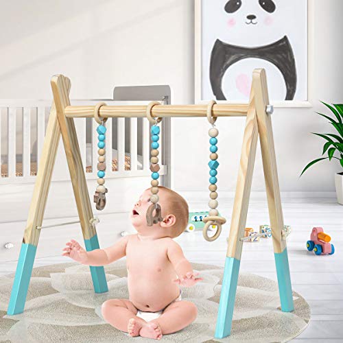 Babygym Tre med hengende rangler i blått, beige og hvitt, baby sitter under og leker på teppe.