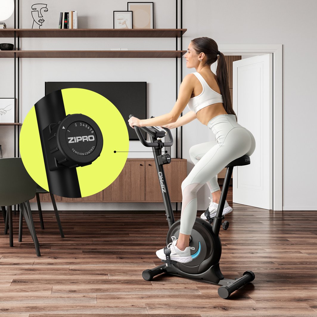 Ergometersykkel med justerbart sete, styrekonsoll og synlig motstandsjustering, plassert i moderne stue.
