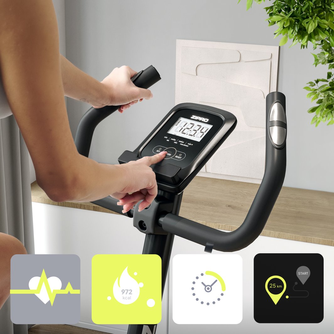 Treningssykkel med digitalt display, svart og sølv, person justerer innstillinger, fire måleikoner vises.