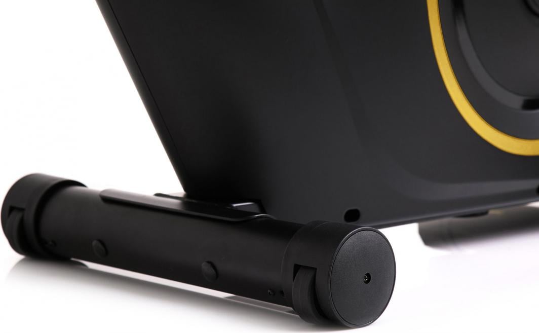 Ergometersykkel med sort metallrør, avrundede ender og små hjul, sett fra siden med gule detaljer.