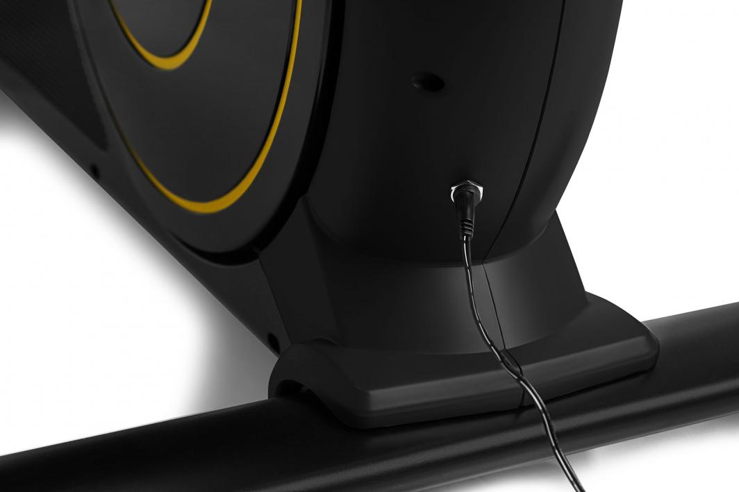 Orbitrek sort og gul base med rund detalj og strømkabel koblet til, sett fra siden med fokus på tilkobling.