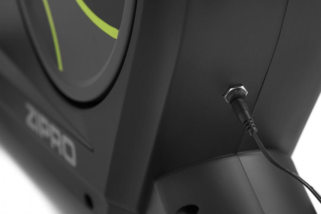 Ergometersykkel med sort og grønn design, synlig strømkabel og nærbilde av kontakt på siden, ZIPRO-logo delvis synlig.