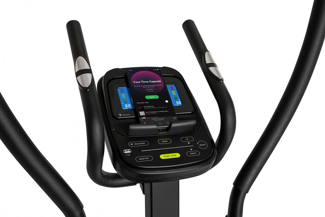 Orbitrek med digitalt display, sorte håndtak med sølvsensorer og mobiltelefon i holder sett forfra.