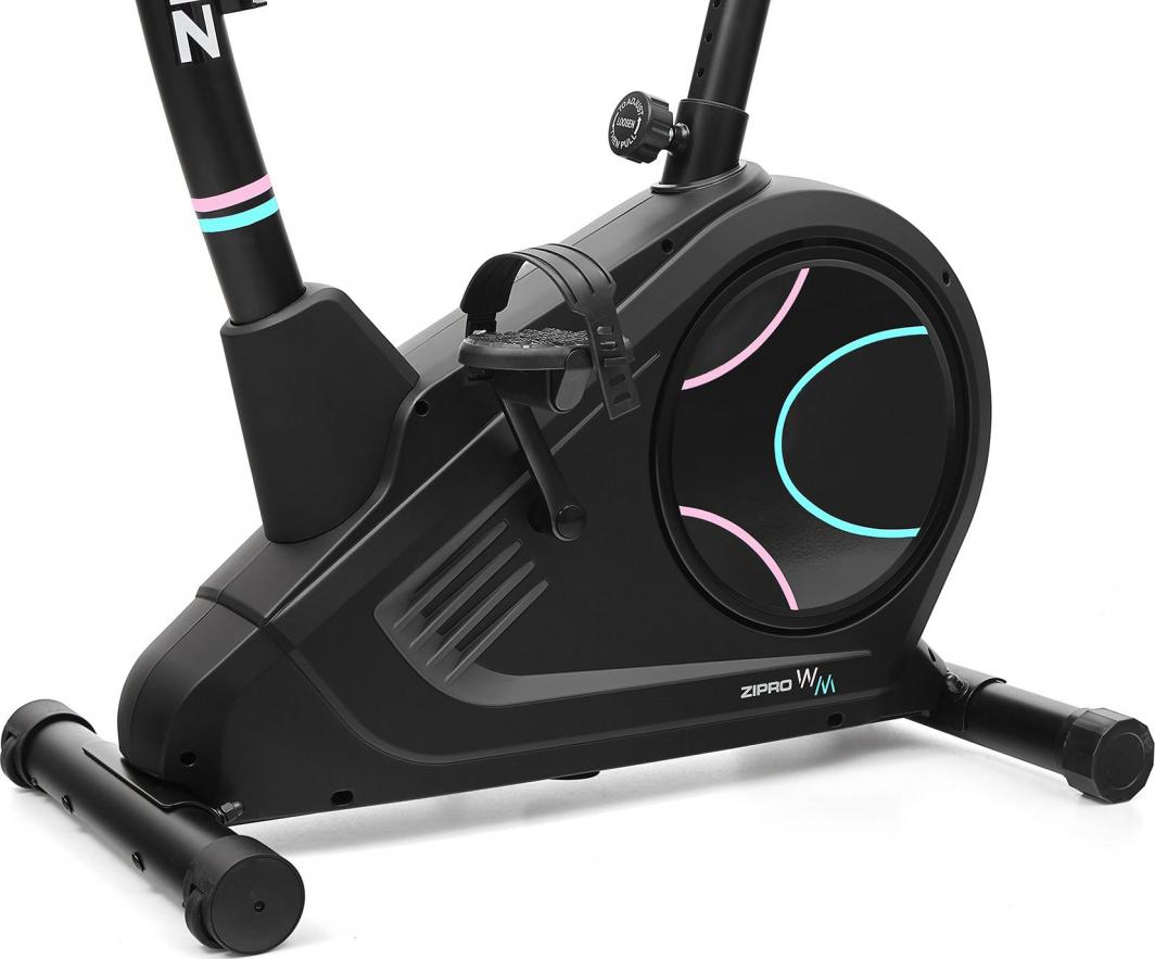 Ergometersykkel i svart med rosa og blå detaljer, nærbilde av pedal med stropp, svinghjul og stabiliserende ben.