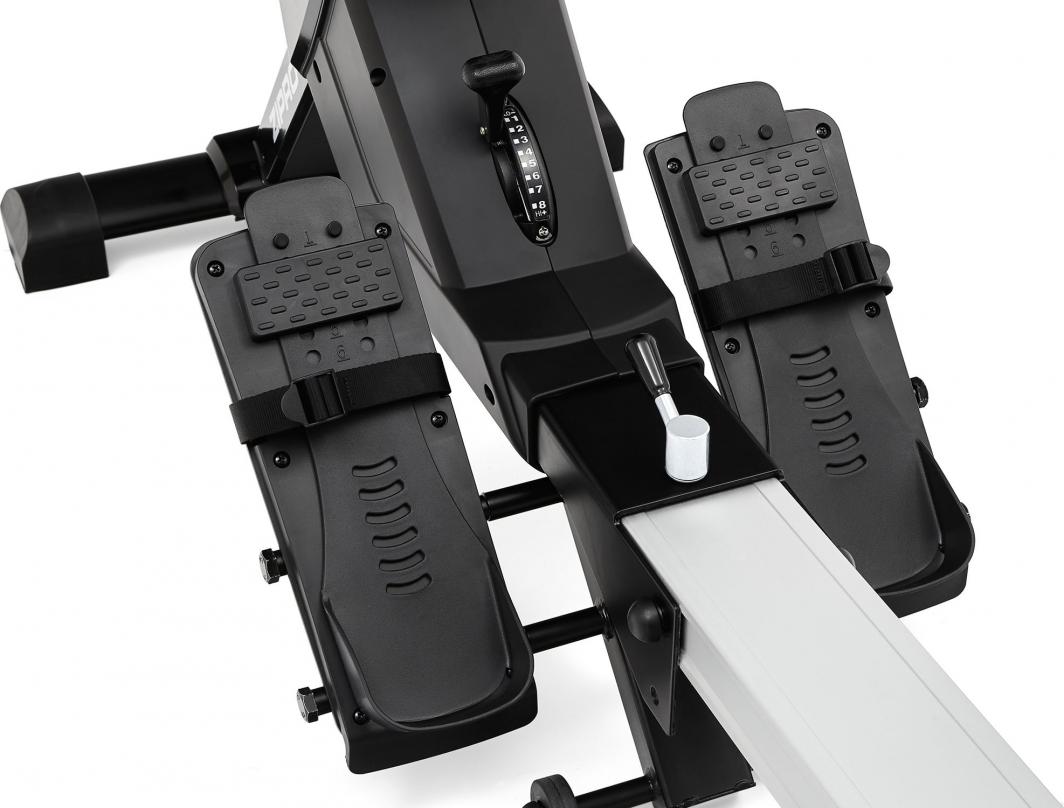 Romaskin Trening med to svarte fotplater, justerbare reimer, midtstilt motstandsjustering og metallskinne.