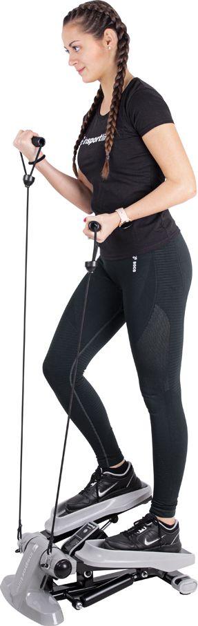 Mini Stepper i grått og svart med pedaler og ekspanderstrikker, brukt av en person, sett fra siden.