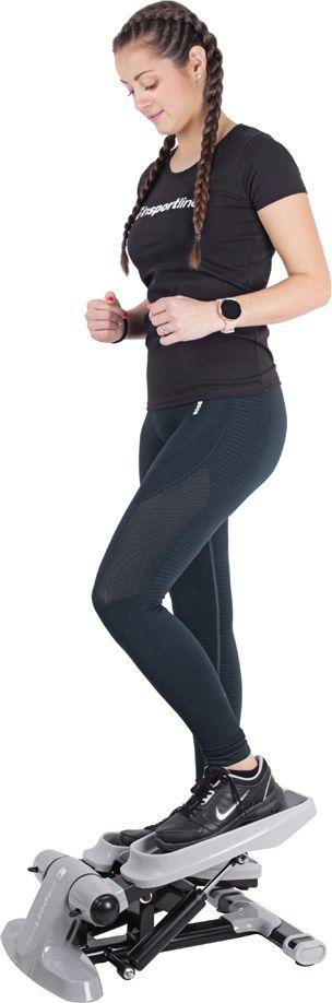 Stepmaskin i grått og svart brukes av kvinne som tråkker på pedalene, sett fra siden. Kompakt design.