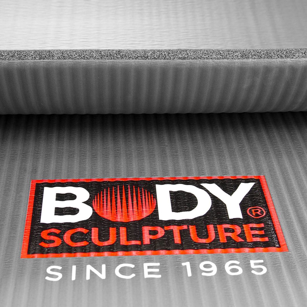 Gymmatte i grått skum med strukturert overflate, detalj av Body Sculpture-logo i hvitt, sort og rødt fra skrå vinkel.