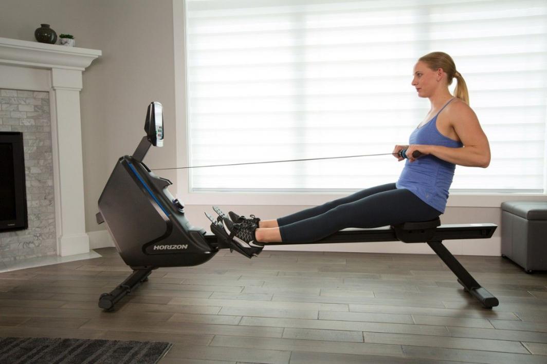 Romaskin Trening sort modell med blå detaljer, kvinne viser ro-øvelse, digital skjerm synlig fra siden.