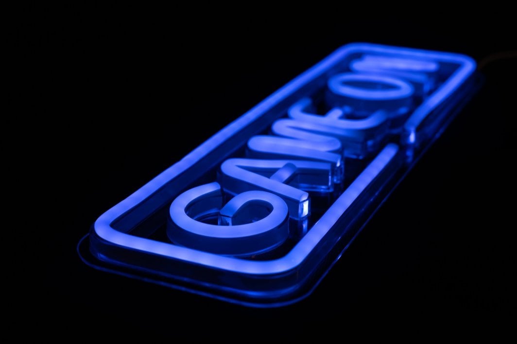 Tredemølle hjemme neonskilt GAME ON i blått LED-lys, skrå nærbilde med akryl og sort bakgrunn.