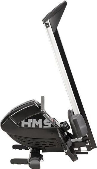 Romaskin i sort og sølv metall sett fra siden, med synlige fotpedaler, sete og HMS-logo på oppreist søyle.