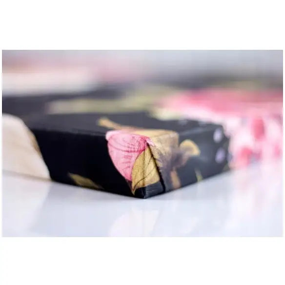 Abstrakt gull og blått lerretsbilde, nærbilde av hjørne med rosa og gult blomstermotiv mot svart bakgrunn.