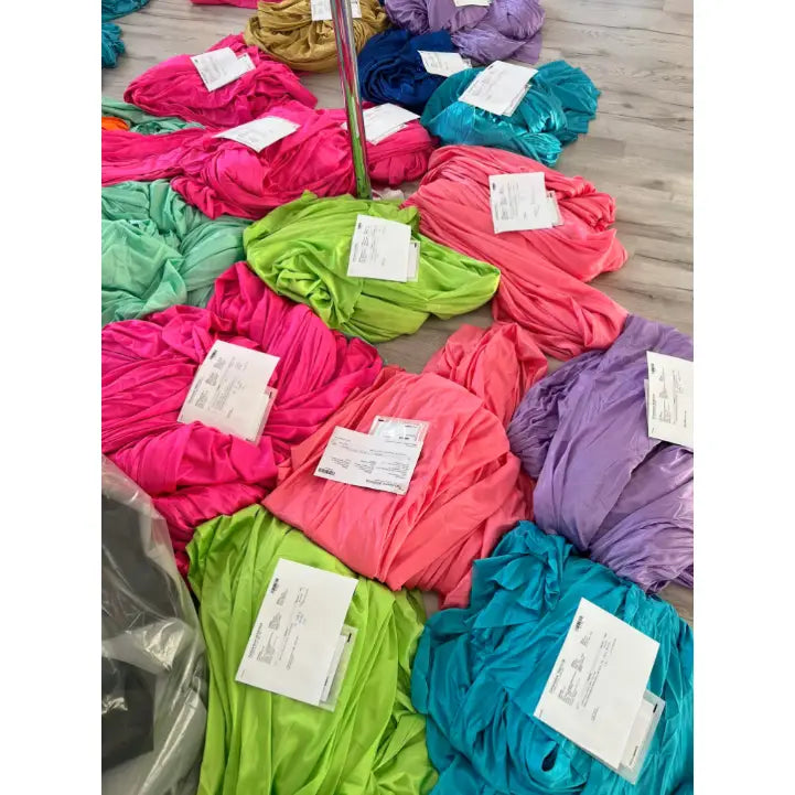 Akrobatisk silkesjerf i rosa, grønn, lilla og blå, sammenrullet med etiketter på lyst gulv.