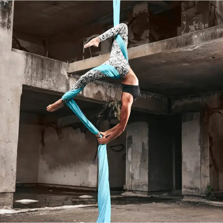 Akrobatisk silkesjerf i lyseblått, person utfører luftakrobatikk og demonstrerer fleksibilitet i industrimiljø.