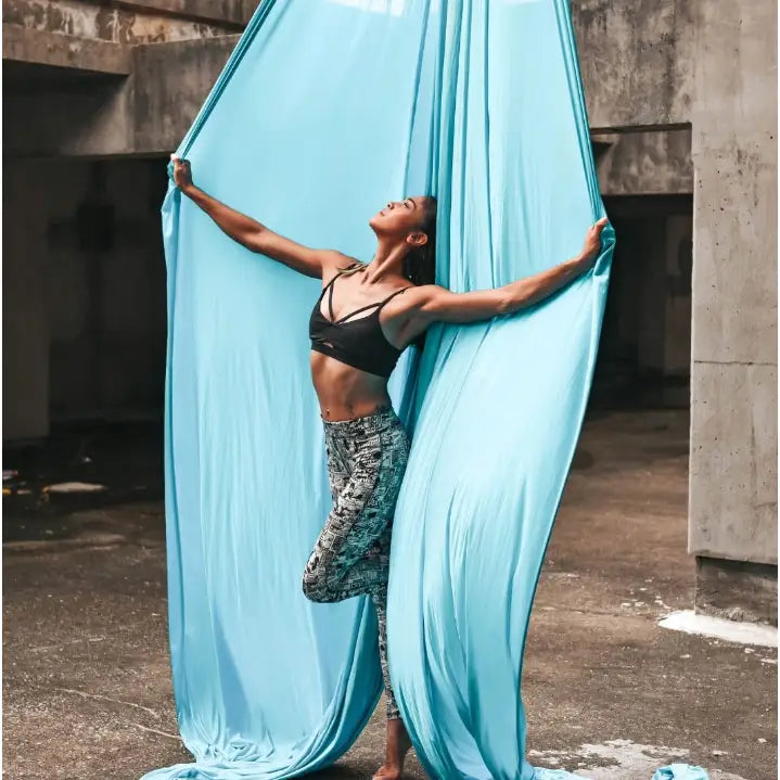 Akrobatisk silkesjerf i lyseblått, henger fra taket mens en person utfører yogastilling i urbant betongmiljø.