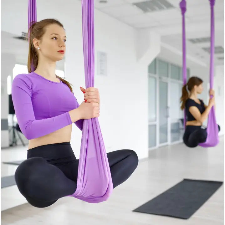 Akrobatisk Silkesjerf Aerial Silk 7 meter, kvinne sitter i lilla yogahengekøye i lyst treningsrom, sidevisning.