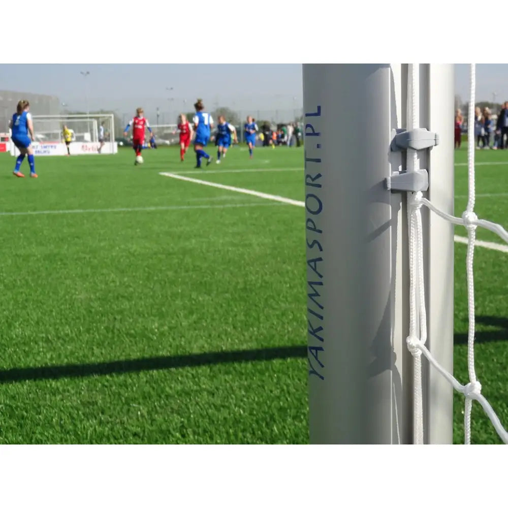Aluminium fotballmål 5 x 2 m, sidevisning med nett, hvit stolpe med "YAKIMASPORT.PL", kunstgress og spillere bak.