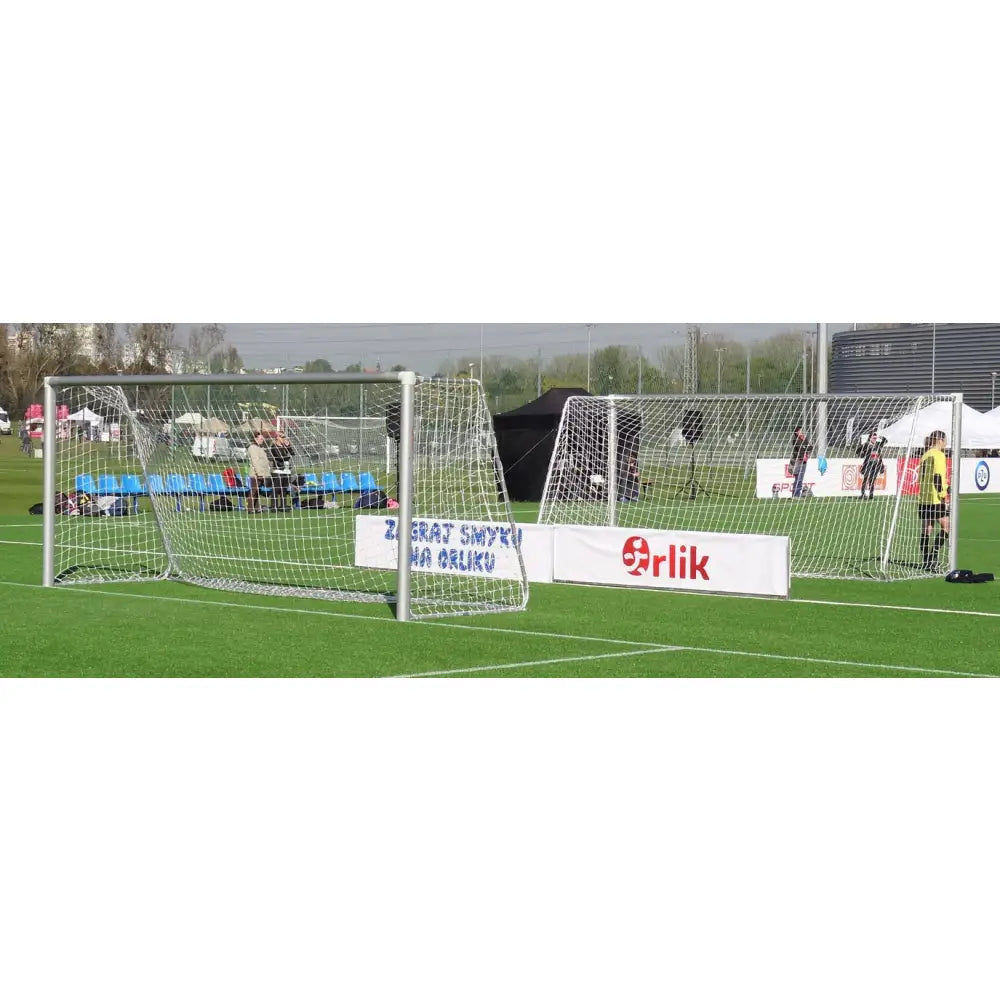 Aluminium fotballmål 5 x 2 m, sidevisning av to mål med hvitt nett på kunstgressbane, blå seter bak.