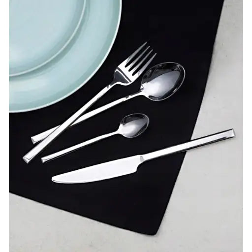 Ambition Como bestikksett, fire deler i blankt stål vist ovenfra på sort serviett ved blå tallerken.