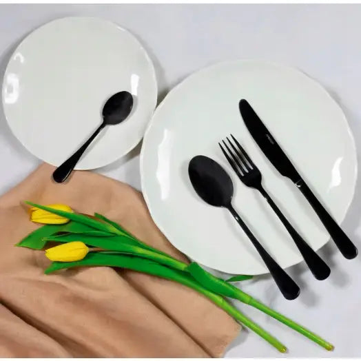 Ambition Enna svart bestikksett på hvite tallerkener, beige serviett og to gule tulipaner ved siden av.