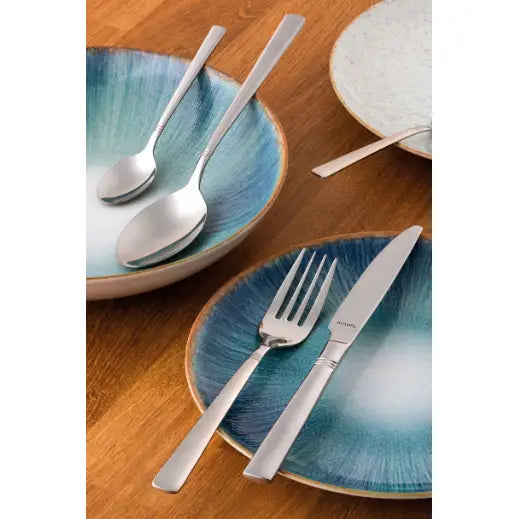 Amefa Dakota bestikk i rustfritt stål, fire deler dandert på blå-grønnmønstrede tallerkener, sett ovenfra.