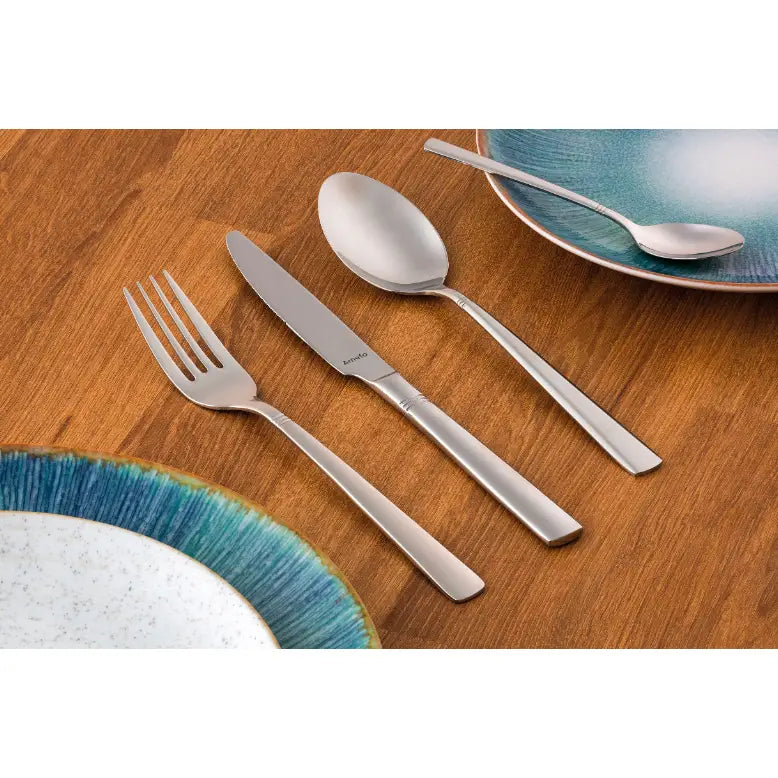 Amefa bestikksett i matt rustfritt stål, gaffel, kniv og skje arrangert på trebord med fargerike tallerkener.
