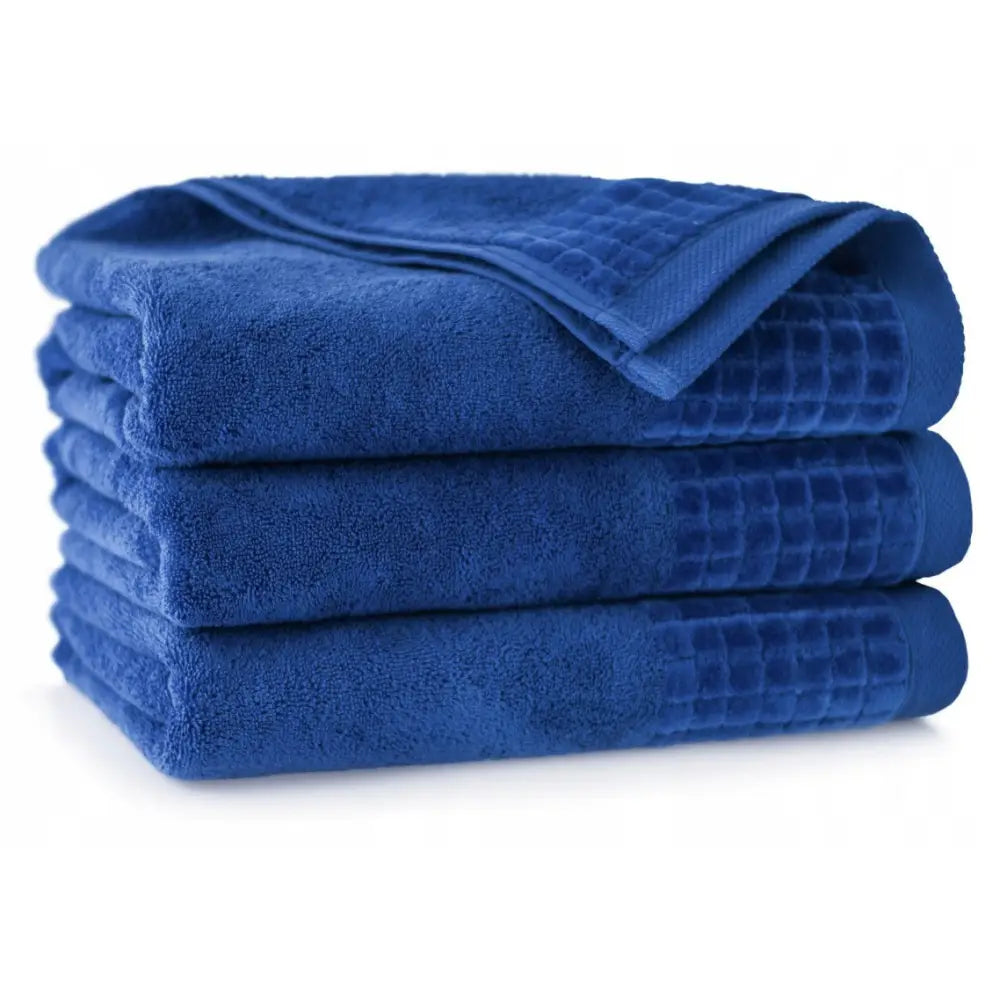 Antibakterielle håndklær Zwoltex, tre mørkeblå håndklær med rutemønstrede ender, stablet fra siden.