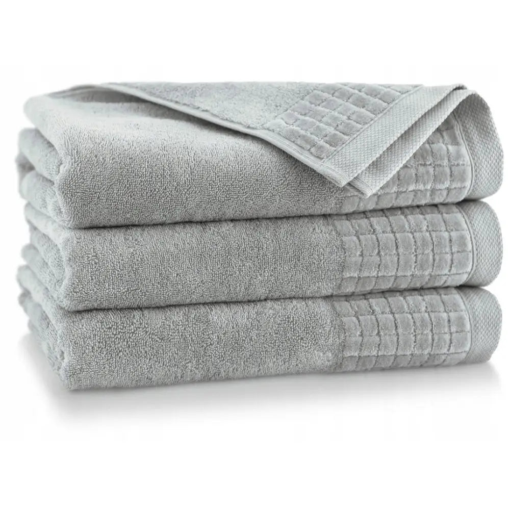 Antibakterielle lysegrå håndklær i bomull, sett med tre stykker med rutemønstret kant stablet sammen.